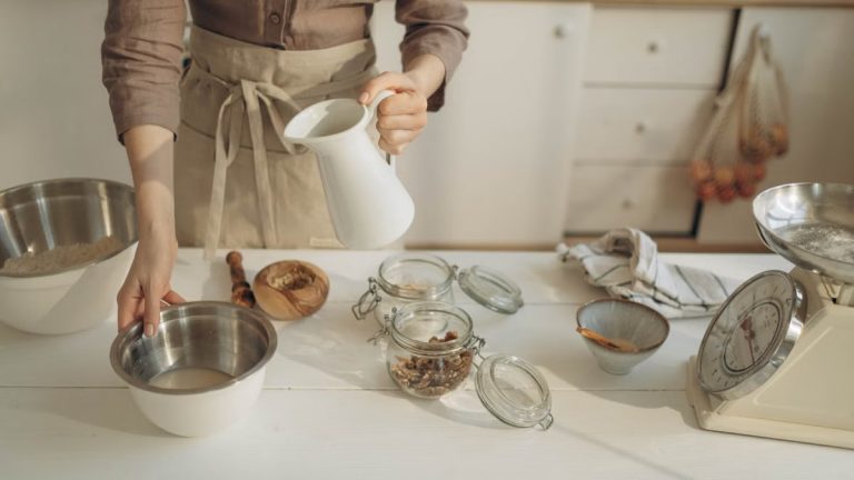 Woman pouring milk into a bowl with various baking ingredients on a kitchen counter.