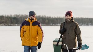 Two men enjoying ice fishing on a frozen lake, equipped with gear.